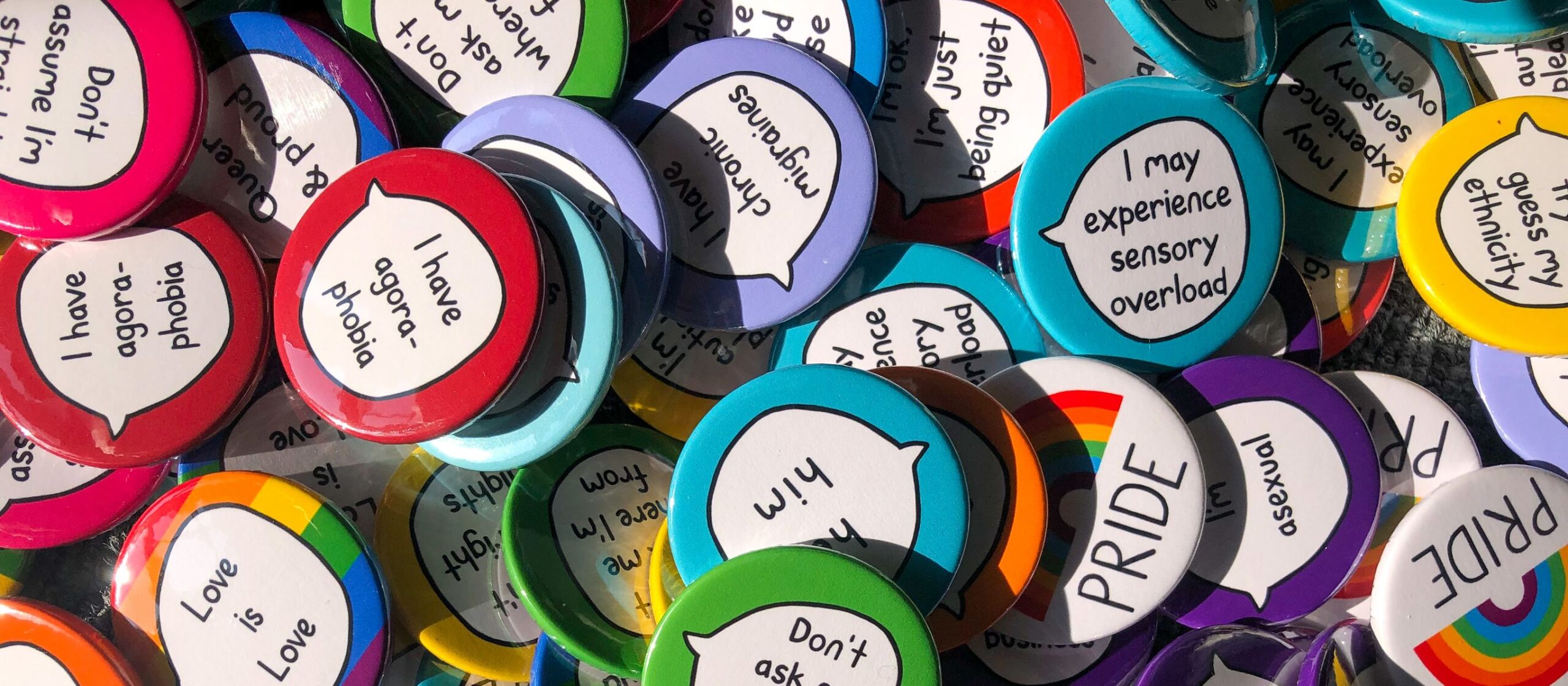 assorted pile of pin badges with personal statements on them such as "I have agoraphobia" and PRIDE